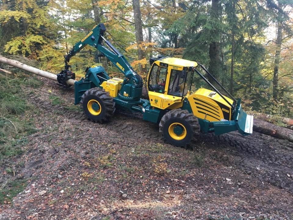 Un tracteur jaune et vert roule sur un chemin de terre dans les bois.
