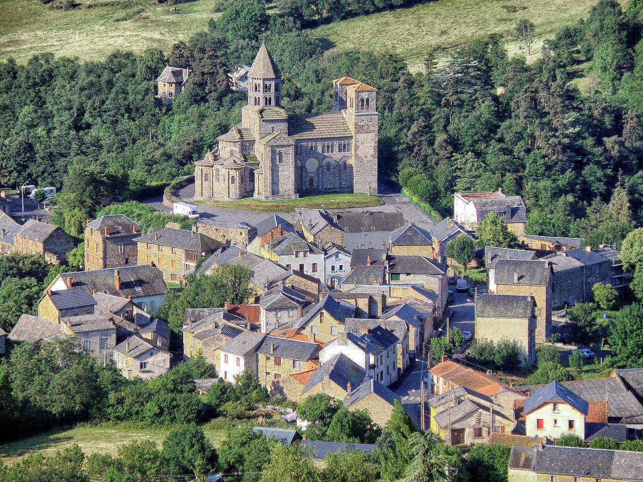 Vue aérienne d'un village historique en pierre en France, dominé par une vieille église romane avec une tour centrale proéminente.