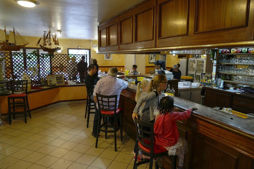 Les clients sont assis à un bar en bois dans un restaurant à la décoration nautique, avec notamment des maquettes de bateaux et un sol carrelé.