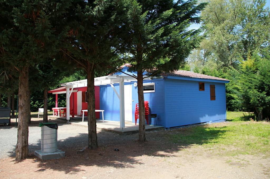 Une petite maison bleue et rouge se dresse au milieu des arbres, dans un cadre boisé et ensoleillé.