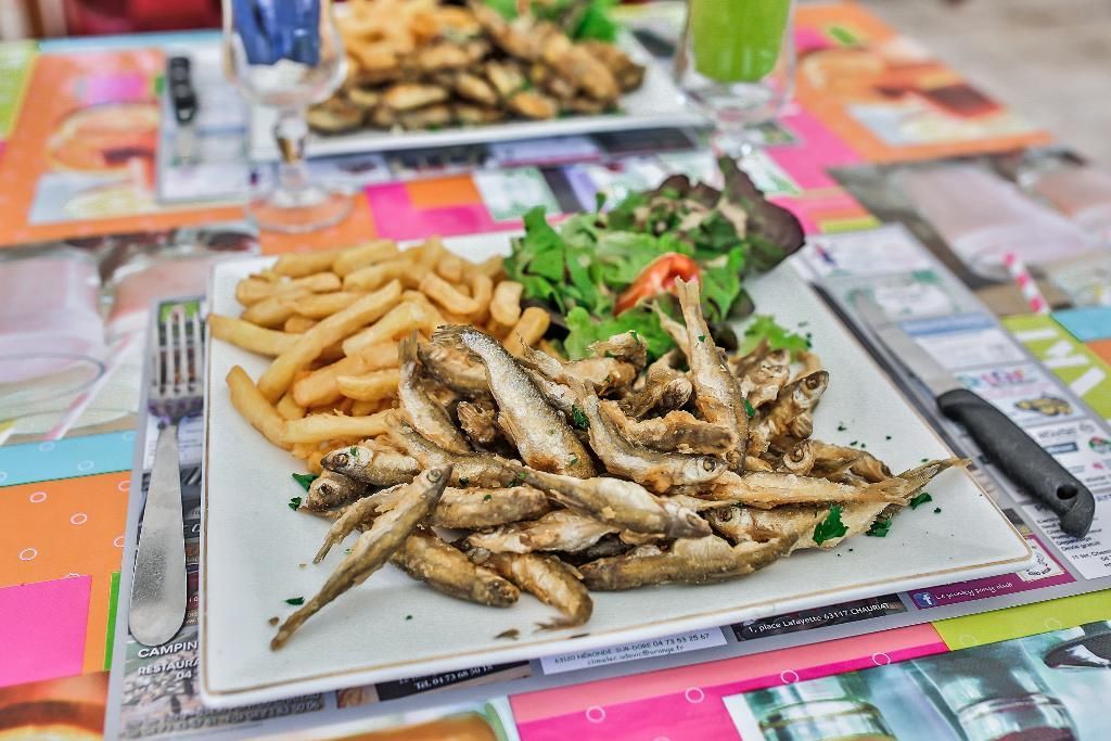 Deux assiettes carrées blanches d'éperlans frits croustillants, servies avec des frites dorées et une salade verte fraîche sur une table colorée.
