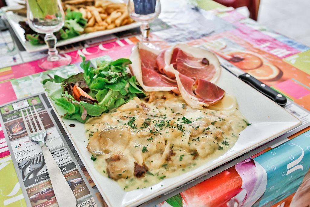 Une assiette carrée présente des pâtes crémeuses aux champignons, au prosciutto et à la verdure fraîche, servies sur une table aux motifs colorés.