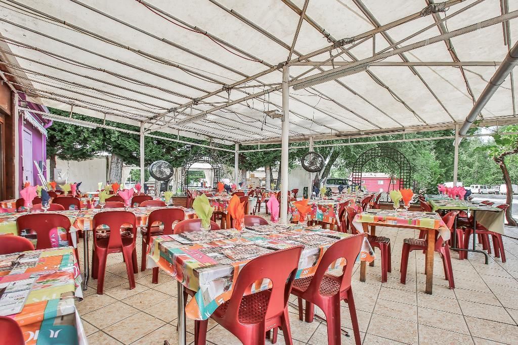 Une terrasse de restaurant en plein air avec des chaises et des tables rouges sous un auvent blanc, décorée de décorations en papier coloré.