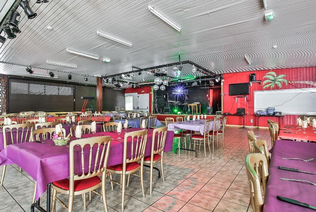 Une salle à manger avec de longues tables recouvertes de nappes violettes et des chaises rouges, aménagée pour un événement avec une scène et des lumières disco.