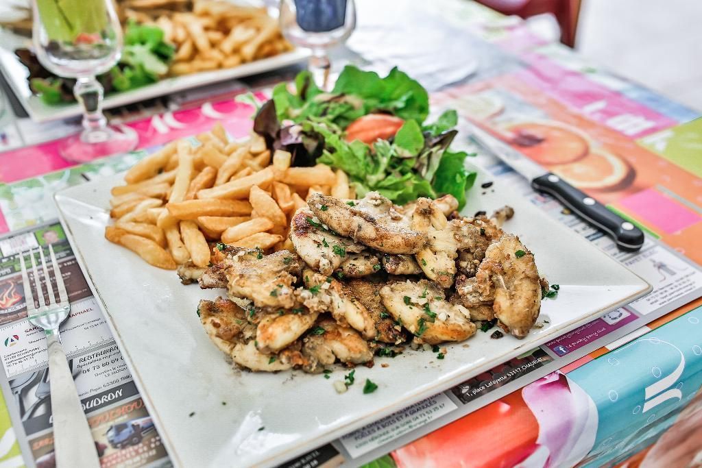 Une assiette de poulet grillé aux herbes, servie avec des frites dorées et une salade fraîche, sur une table joliment décorée.