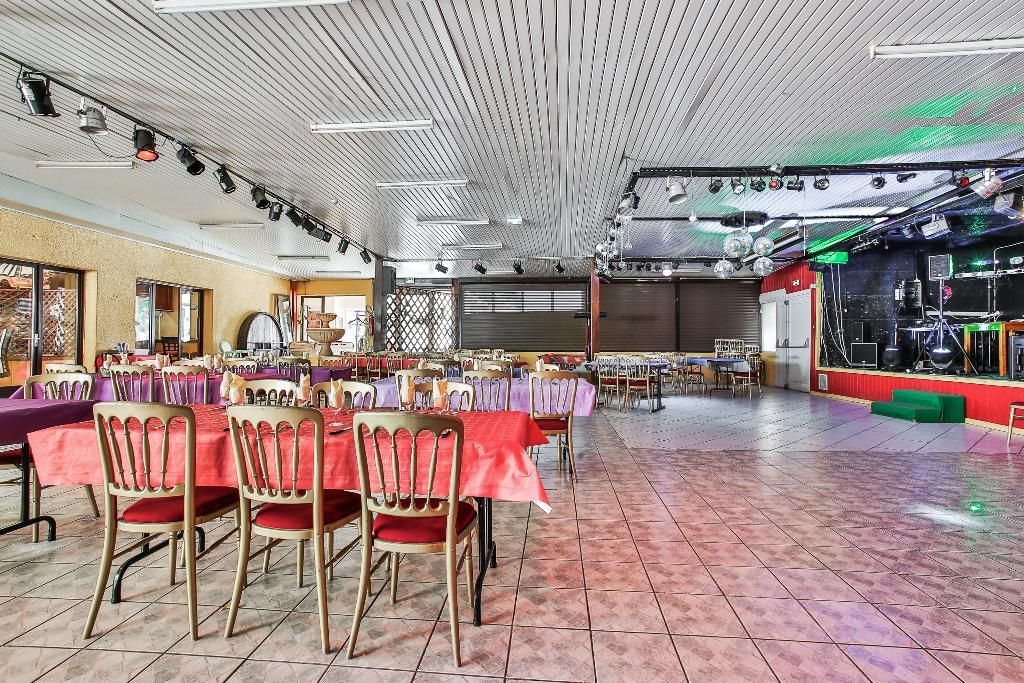 Vue panoramique d'une salle de banquet avec des tables nappées de rouge, des chaises, un sol carrelé et un éclairage de scène décoratif.