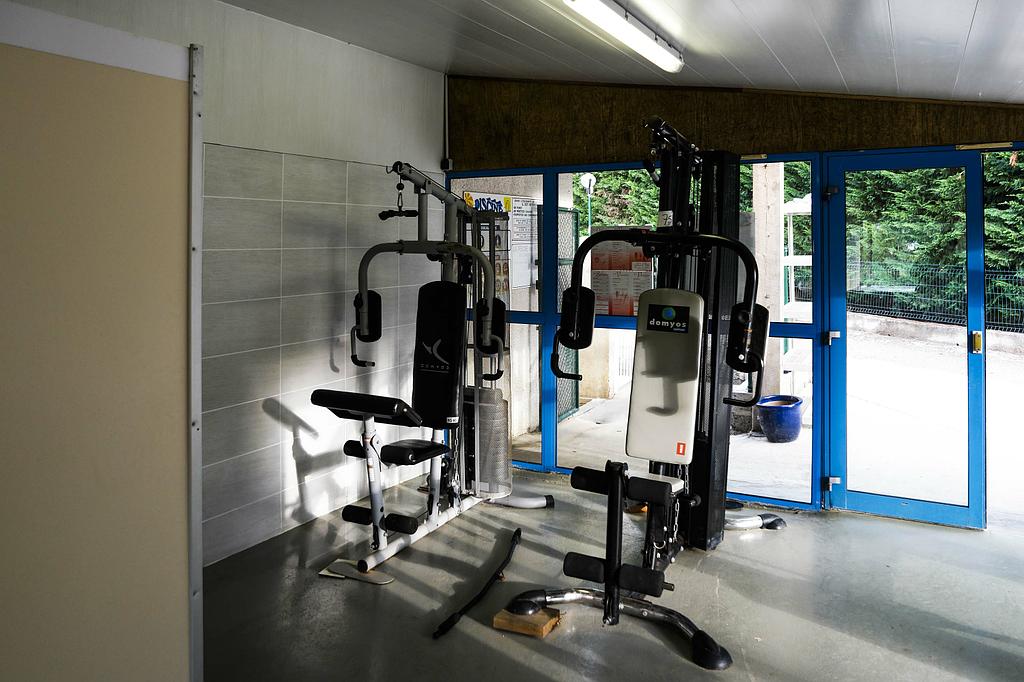 Deux appareils de musculation pour salle de sport à domicile sont installés sur un sol en béton dans une pièce dotée de grandes portes vitrées à cadre bleu donnant sur l'extérieur.