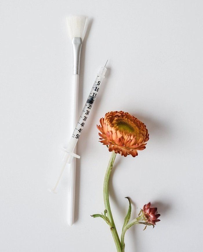Pincel, jeringa y flor de naranja sobre fondo blanco.