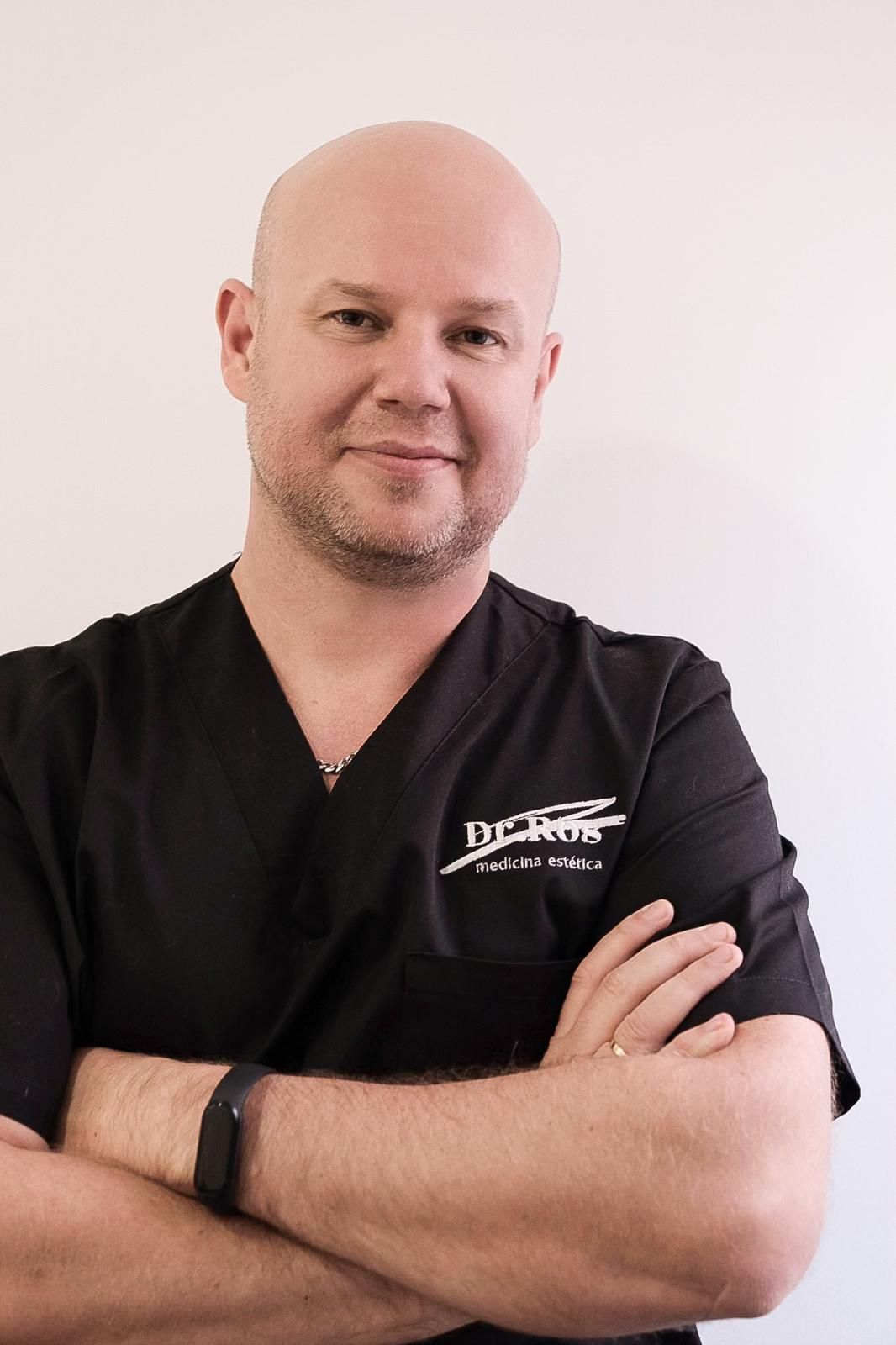 Un hombre calvo con uniforme negro y los brazos cruzados sonríe a la cámara.