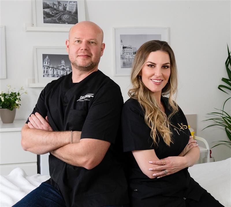 Dos personas, un hombre y una mujer, están de pie, espalda con espalda, sonriendo.