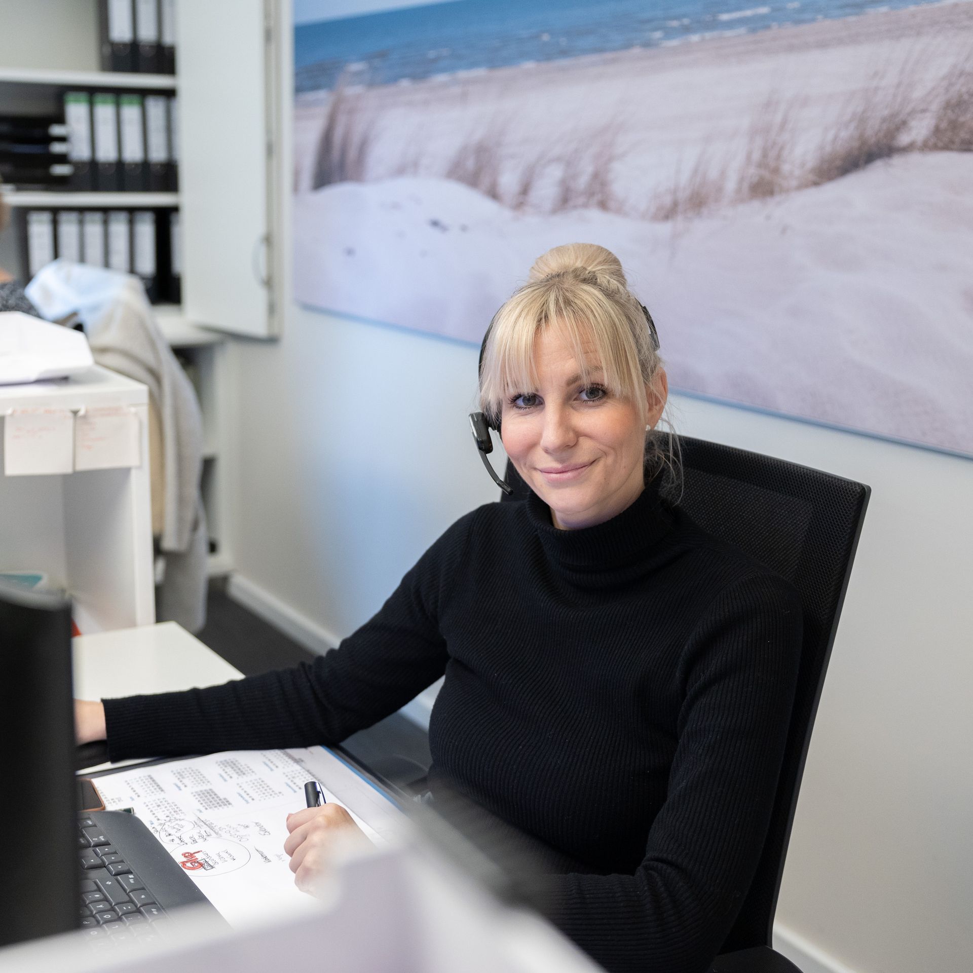 Eine Frau mit Headset sitzt an einem Schreibtisch vor einem Computer