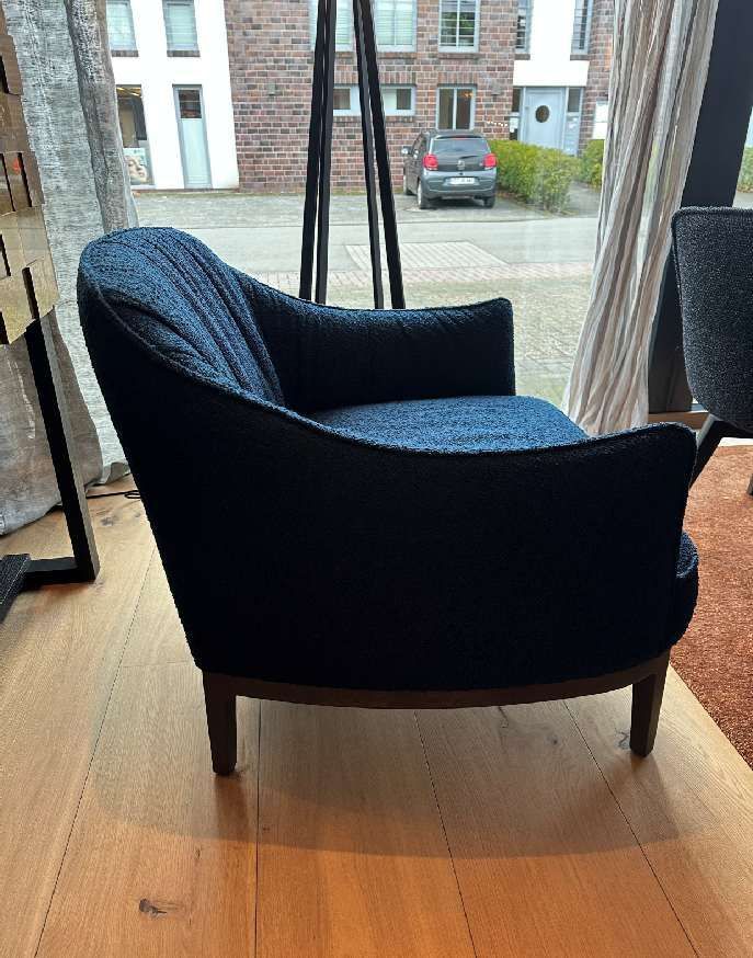 Ein blauer Stuhl steht auf einem Holzboden vor einem Fenster.