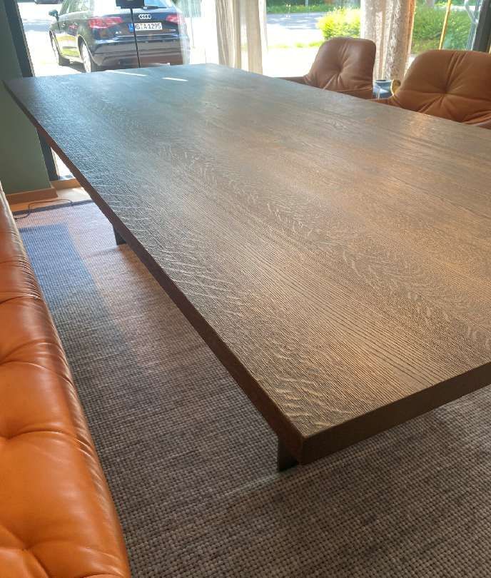 In einem Wohnzimmer steht ein langer Holztisch neben einem Sofa.