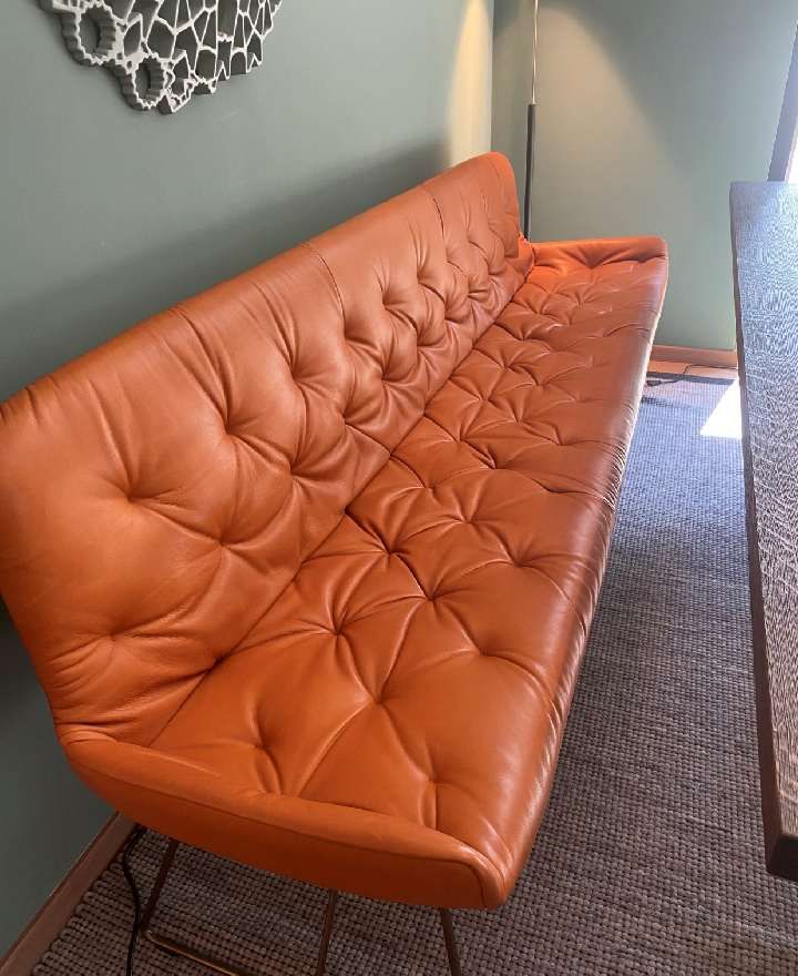 In einem Raum steht neben einem Tisch ein orangefarbenes Ledersofa.