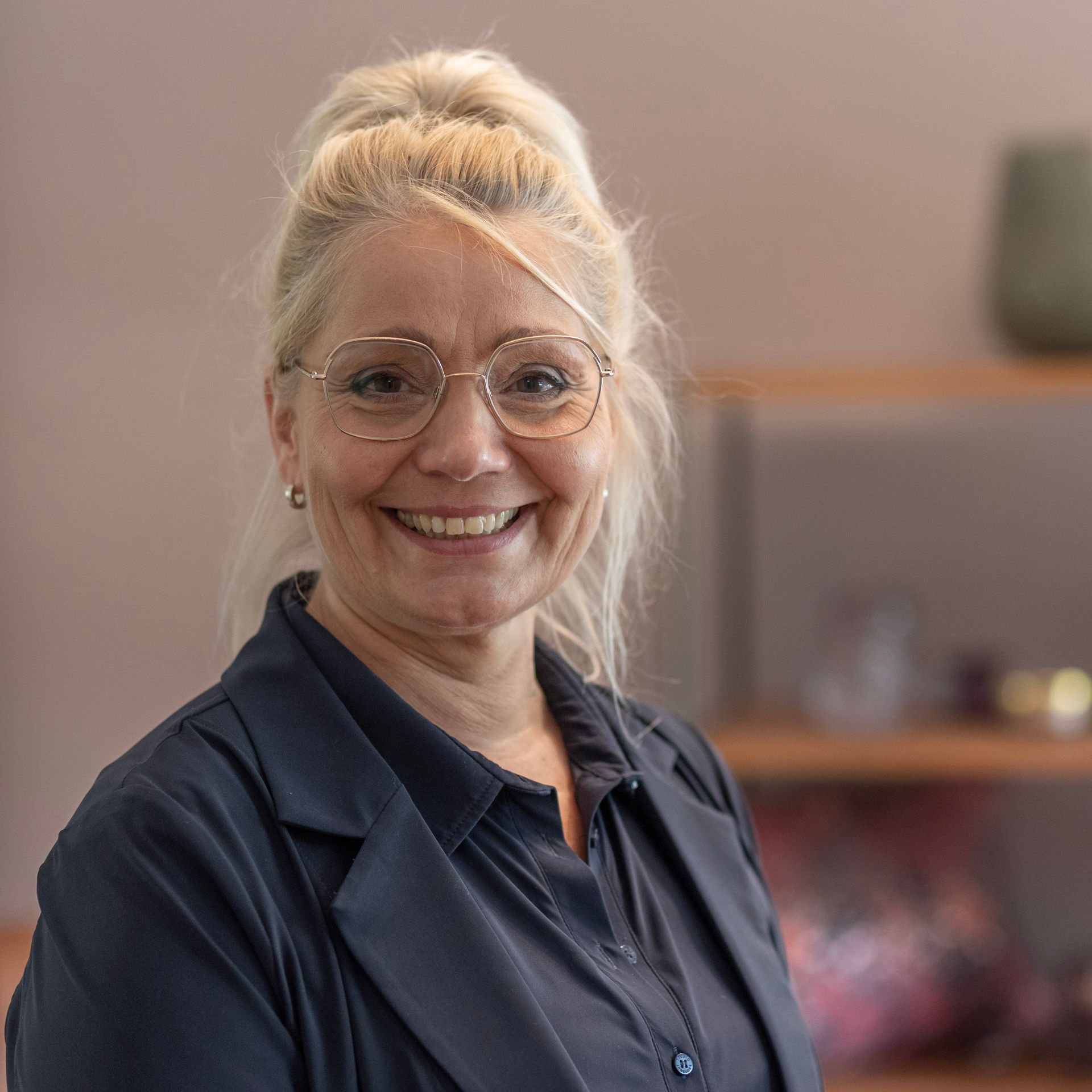 Eine Frau mit Brille und blauem Hemd lächelt in die Kamera.