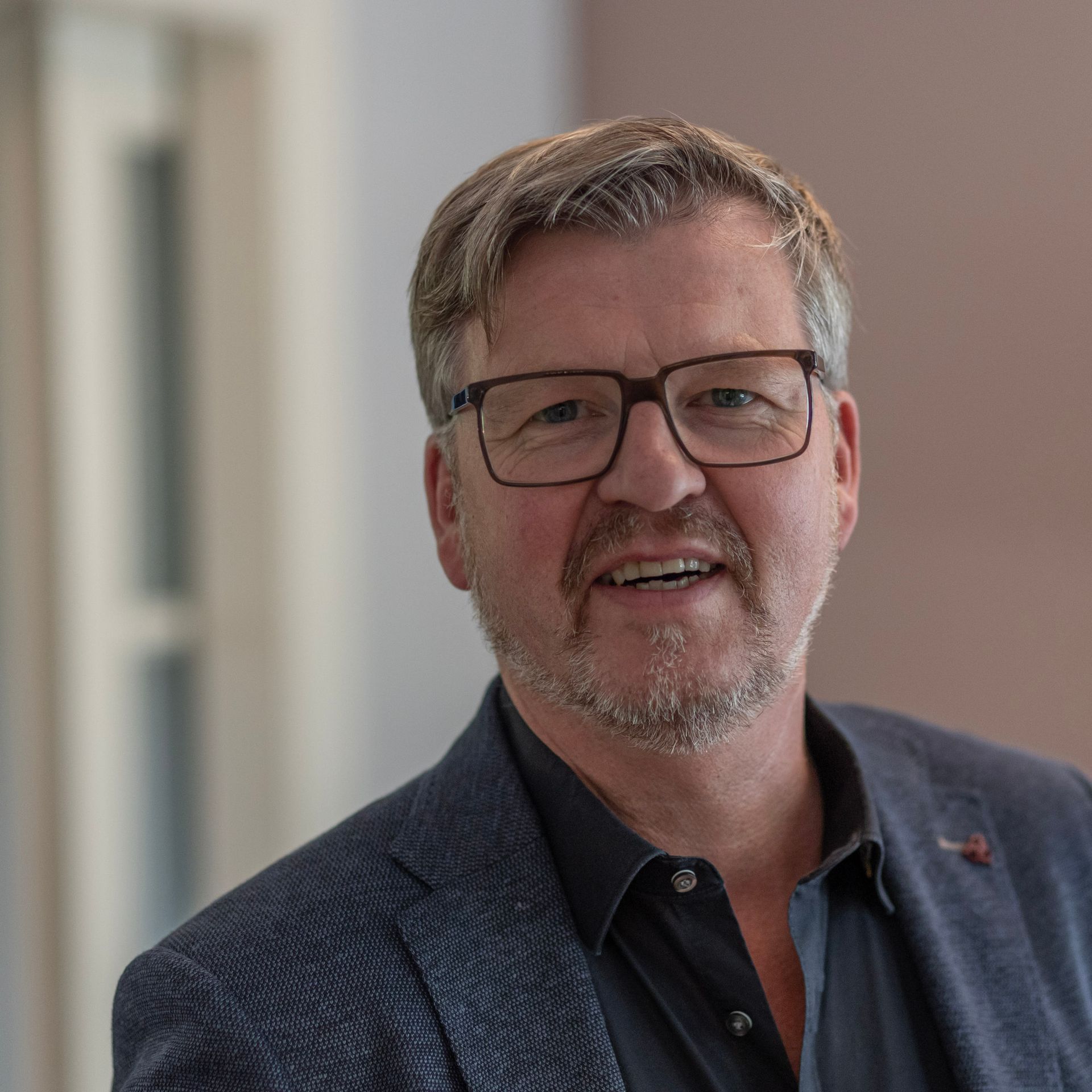 Ein Mann mit Brille und Anzug lächelt in die Kamera.