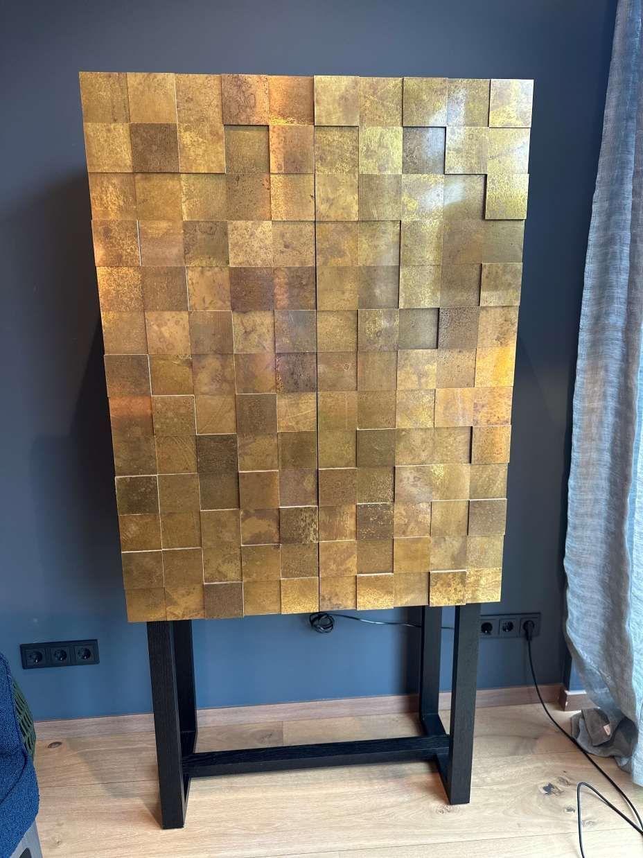 In einem Raum steht auf einem Holzboden ein Messingschrank.