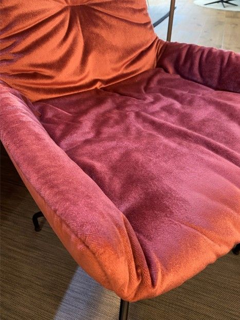 Nahaufnahme eines Stuhls mit weichem, samtartigem Stoff in tiefen Rosa- und warmen Orangetönen.