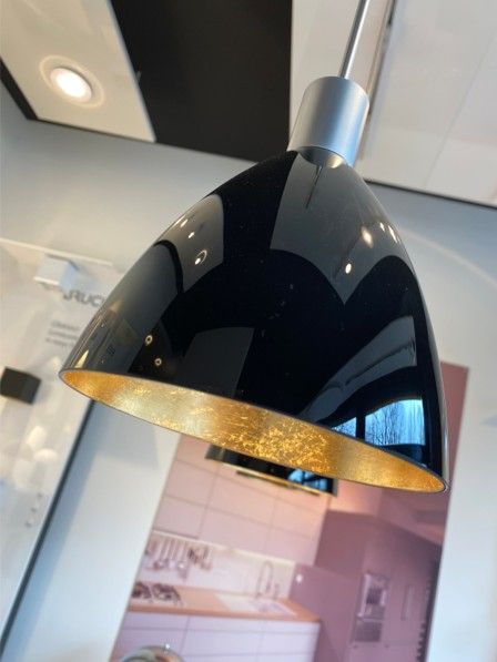 Eine glänzend schwarze Pendelleuchte mit strukturierter goldener Innenseite, die in einem Raum hängt.