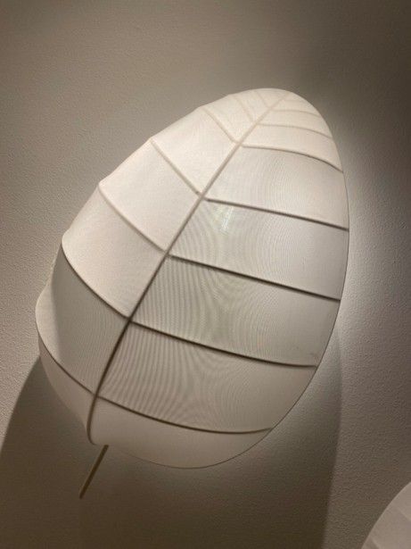 Eine eiförmige Wandlampe mit einem weißen, gittergemusterten Stoffschirm, der ein sanftes, warmes Licht ausstrahlt.