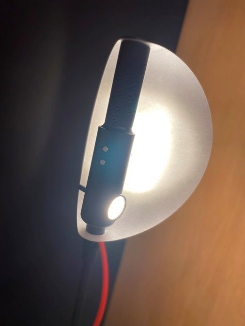 Nahaufnahme einer kleinen, zylindrischen schwarzen Leselampe mit leuchtendem Licht vor einem durchscheinenden weißen Lampenschirm.