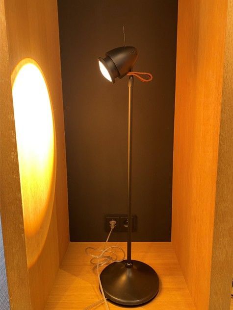 In einer Holznische steht eine schwarze Stehlampe mit Spotlicht, die ein warmes Licht an die Seitenwand wirft.