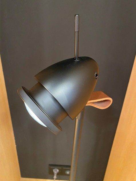 Ein schwarzer Metall-Scheinwerferkopf mit einem kleinen Ledergriff, montiert auf einer dünnen vertikalen Stange.