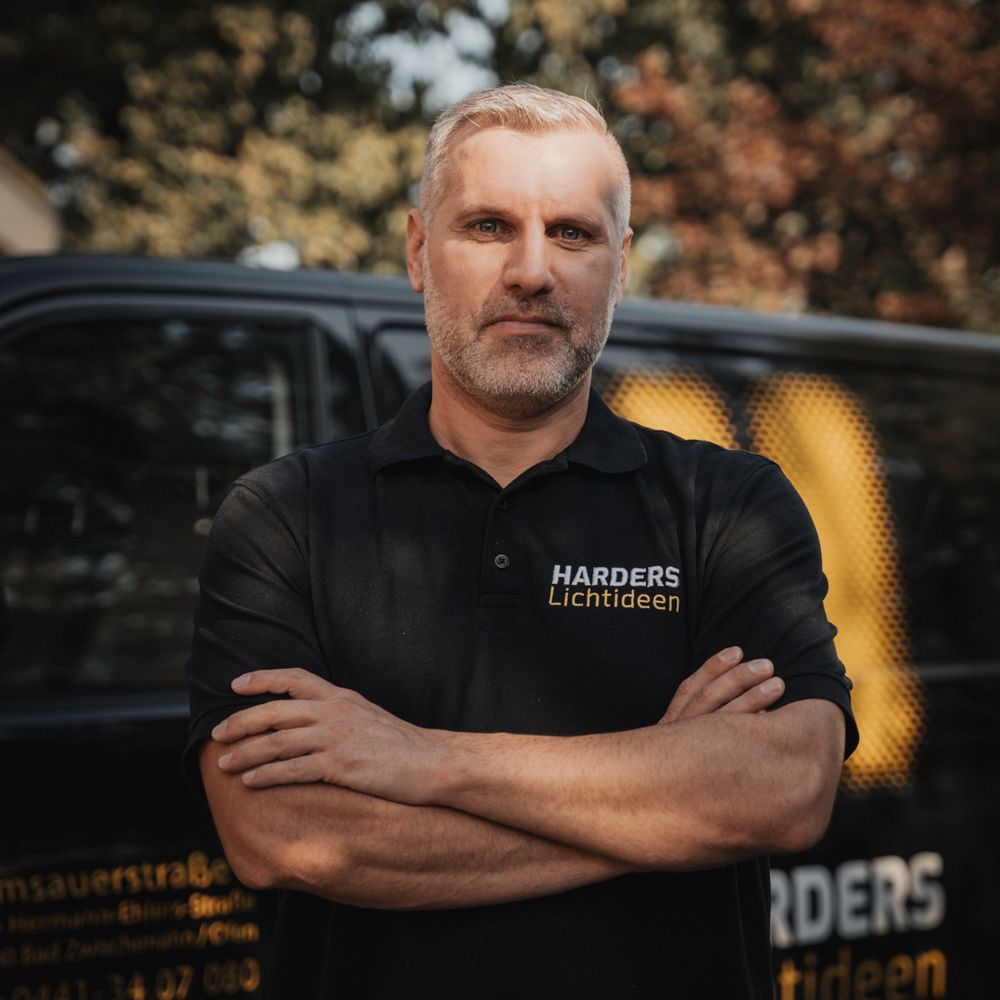 Ein Mann in einem Harders-Shirt steht mit verschränkten Armen da