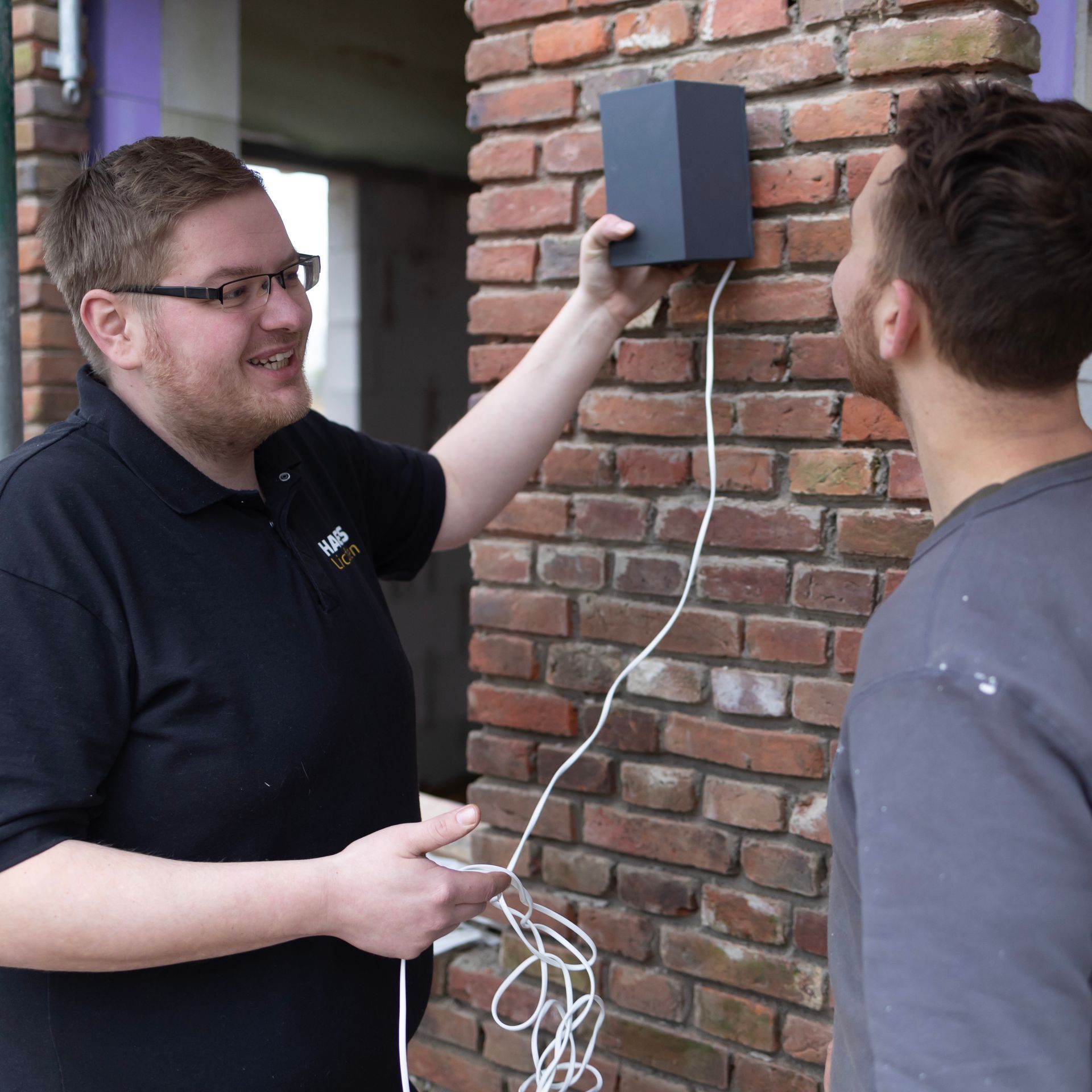 Zwei Männer stehen vor einer Backsteinmauer