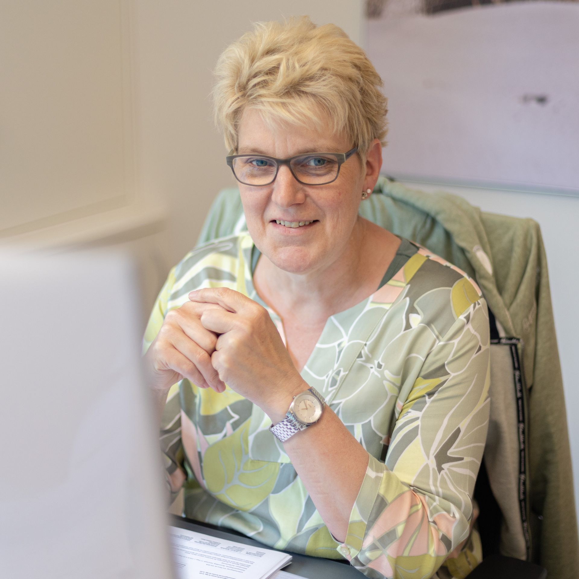 Eine Frau mit Brille sitzt an einem Schreibtisch vor einem Computer.