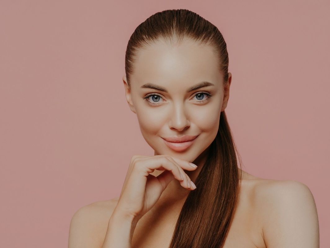 Una mujer con cabello largo sonríe y se toca la cara con la mano.