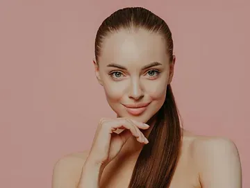 Una mujer con cabello largo sonríe y se toca la cara con la mano.