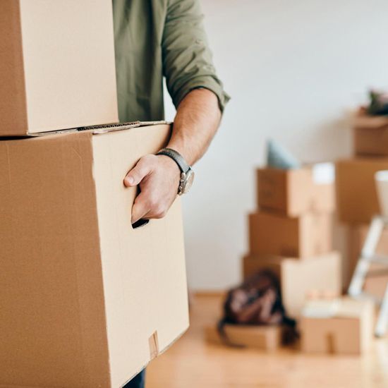 Un hombre lleva una pila de cajas de cartón en una habitación.
