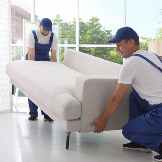 Dos hombres con overoles azules están moviendo un sofá blanco