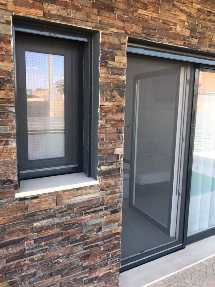 Janela e porta de correr com molduras escuras e telas embutidas na fachada de tijolos.
