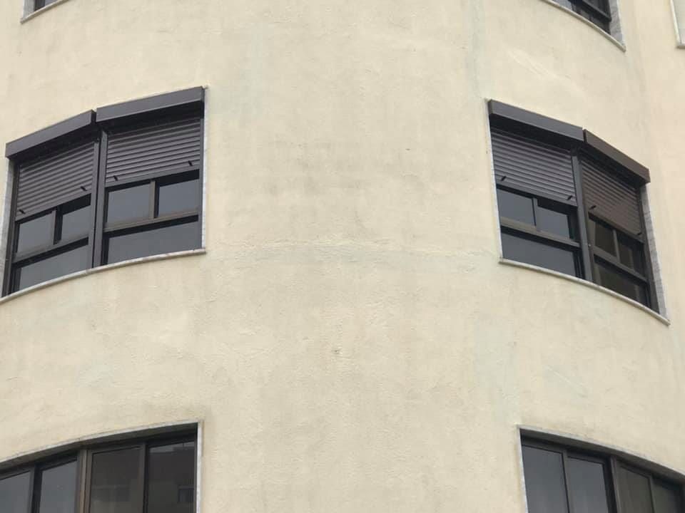 Exterior do edifício em tom bege com janelas curvas e persianas marrom-escuras.