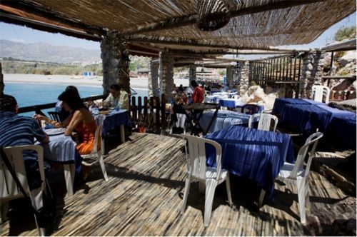 Un grupo de personas están sentadas en mesas en un restaurante con vistas al océano.