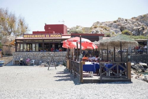 Un restaurante llamado restaurante el peñón tiene mesas y sombrillas afuera