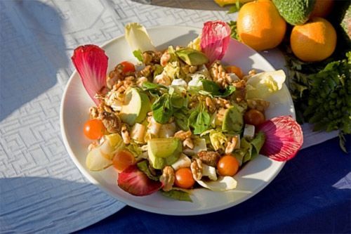 Un plato blanco cubierto con ensalada y fruta sobre una mesa.