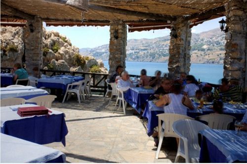 Un grupo de personas están sentadas en mesas en un restaurante con vista a un cuerpo de agua.