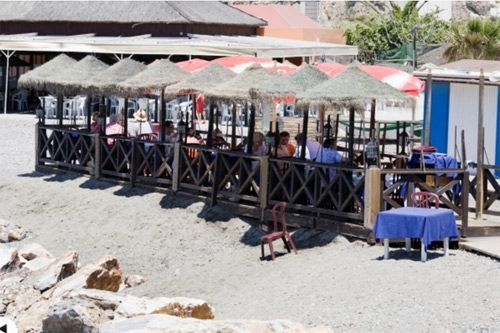 La gente está sentada en mesas bajo sombrillas en la playa.