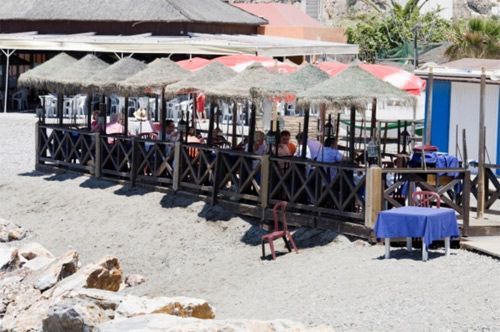 La gente está sentada en mesas bajo sombrillas en la playa.