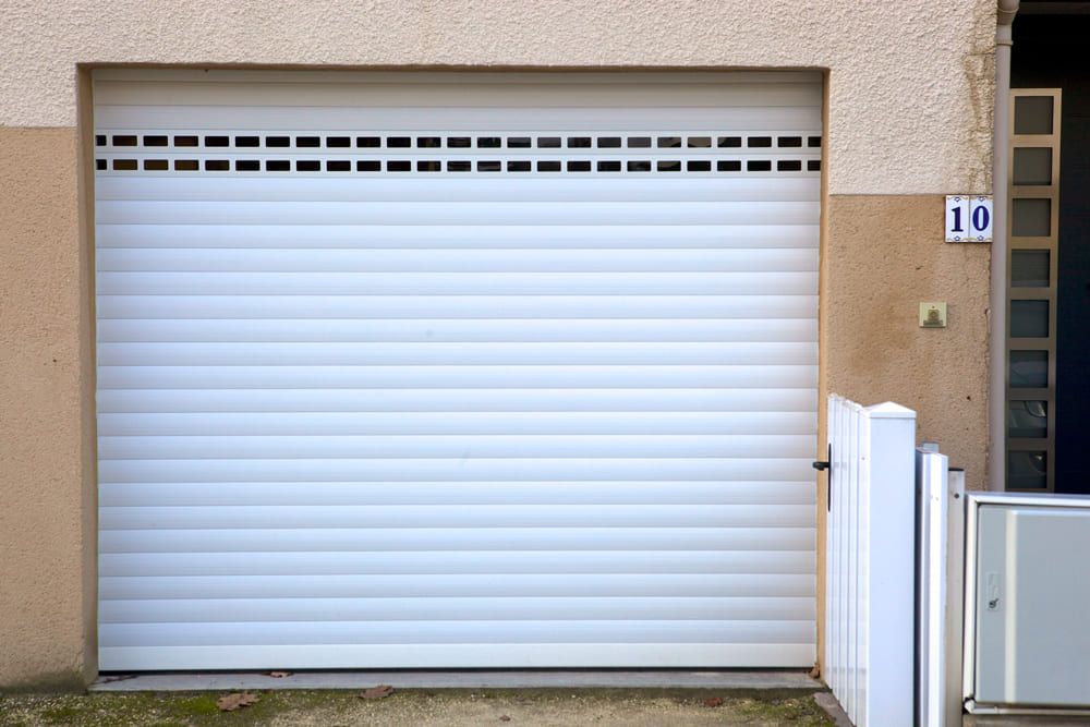 Porte de garage blanche fermée, encastrée dans un mur beige, à côté d'une plaque portant le numéro 10.