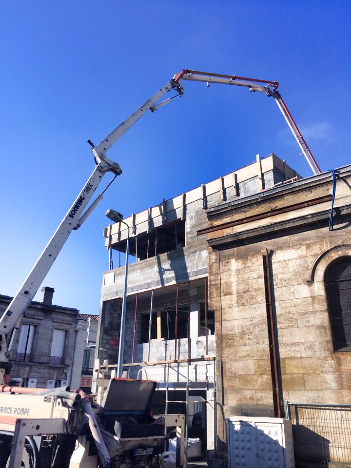 Chantier de construction avec une grue coulant du béton à côté d'un vieux bâtiment en pierre sous un ciel bleu