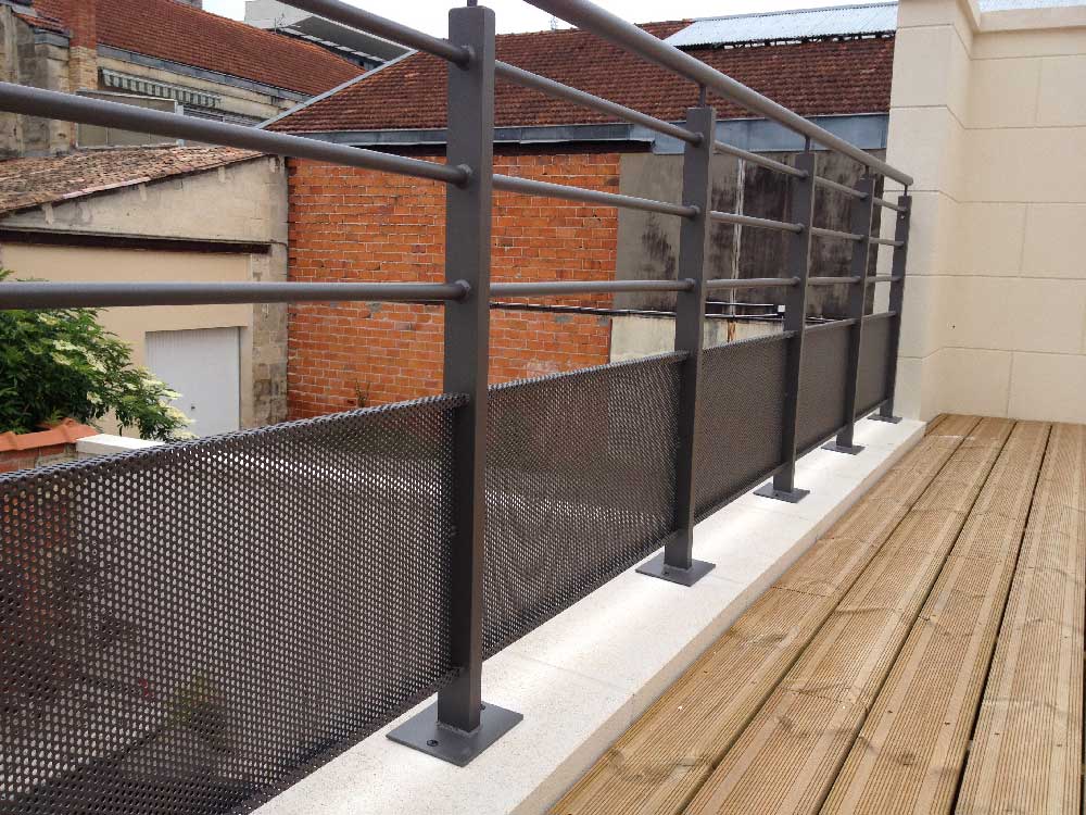Balcon extérieur avec rambarde en métal noir et terrasse en bois jouxtant des bâtiments en briques