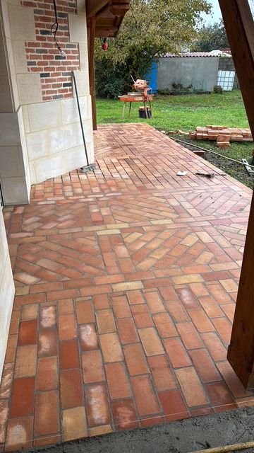 Allée en briques longeant une maison et menant à une cour gazonnée avec un petit abri de jardin en arrière-plan.