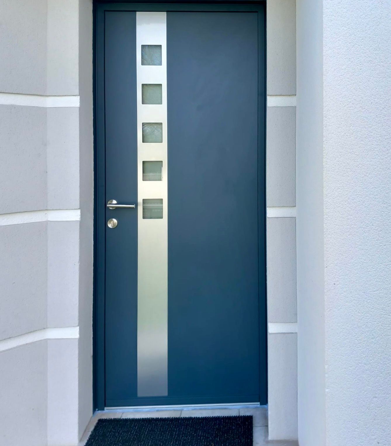 Porte d'entrée bleue avec panneaux verticaux en verre dépoli dans un hall d'entrée clair