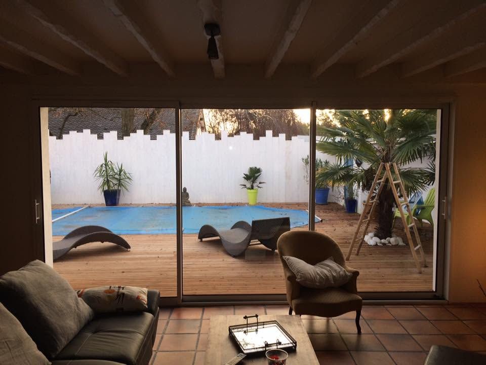 Terrasse couverte avec chaises longues donnant sur une piscine et un petit jardin au-delà des portes coulissantes en verre