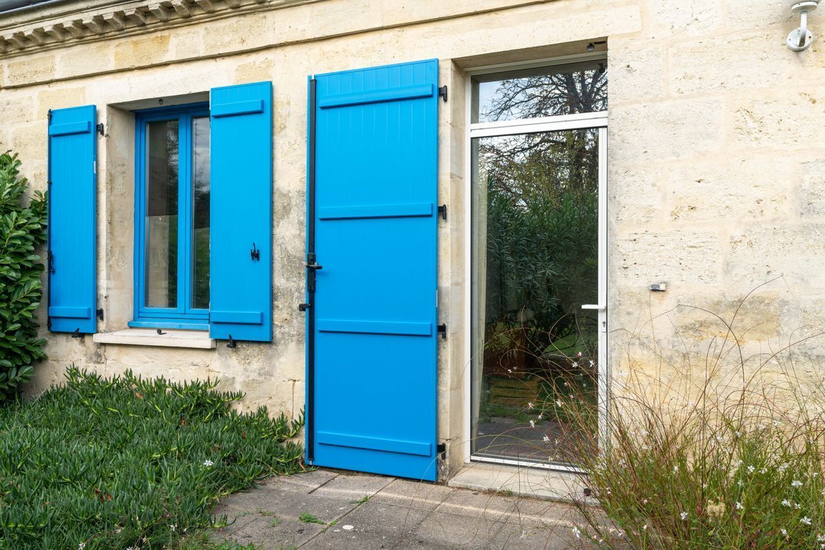 Volets et porte bleus sur une maison en pierre avec un petit jardin et une entrée par patio