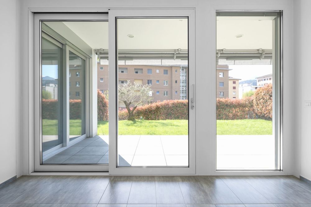 Chambre moderne avec de grandes portes coulissantes en verre s'ouvrant sur un patio lumineux et une cour verdoyante.
